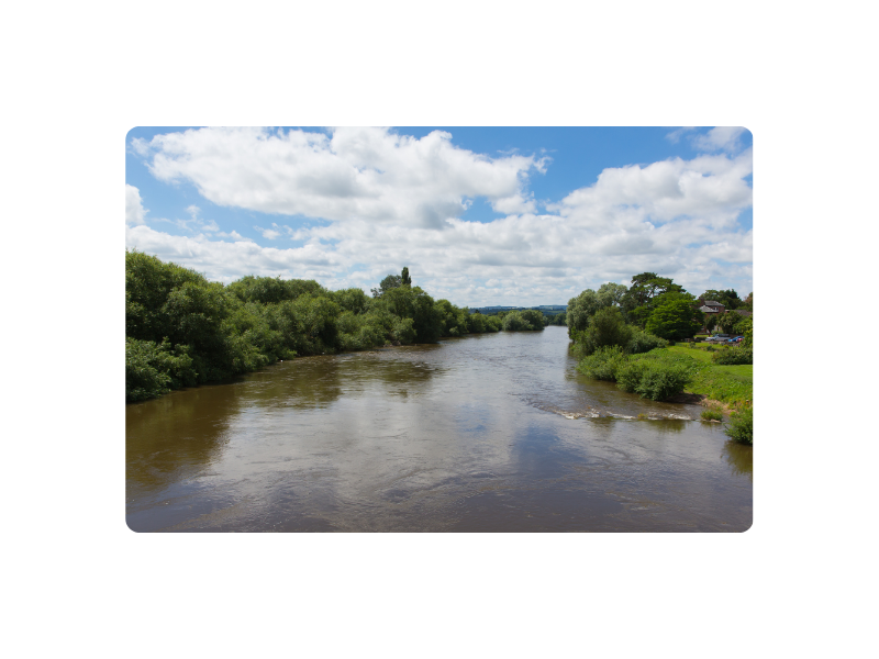 photograph of River Wye, framed by river banks, blue sky and white clouds